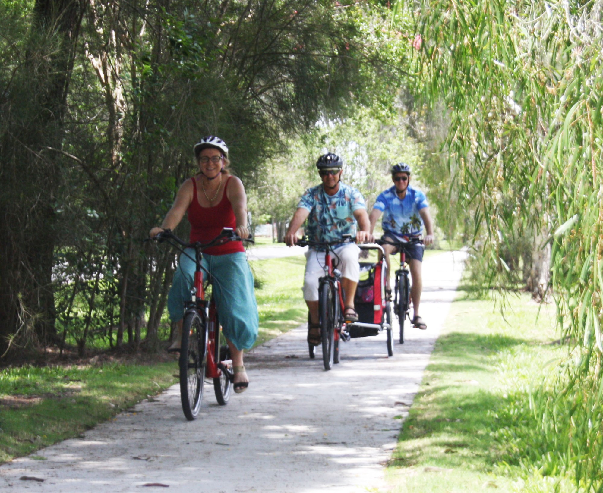 Christmas Family Fun: E-Bike Ride Around Yandina with Grandkids A joyful family Christmas ride on e-bikes around Yandina, with grandparents and a granduncle towing grandkids in a child trailer on tree-lined bike pathways after visiting the Ginger Factory.