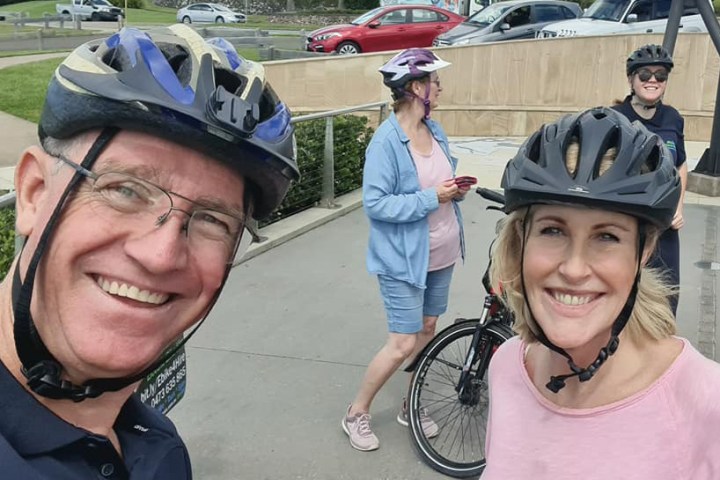 Stuart takes a selfie with Kay McGrath at Alexandra Headland during the River to River e-bike tour hosted by EcoTekkSC, with other participants smiling in the background at the HMAS Brisbane Memorial.
