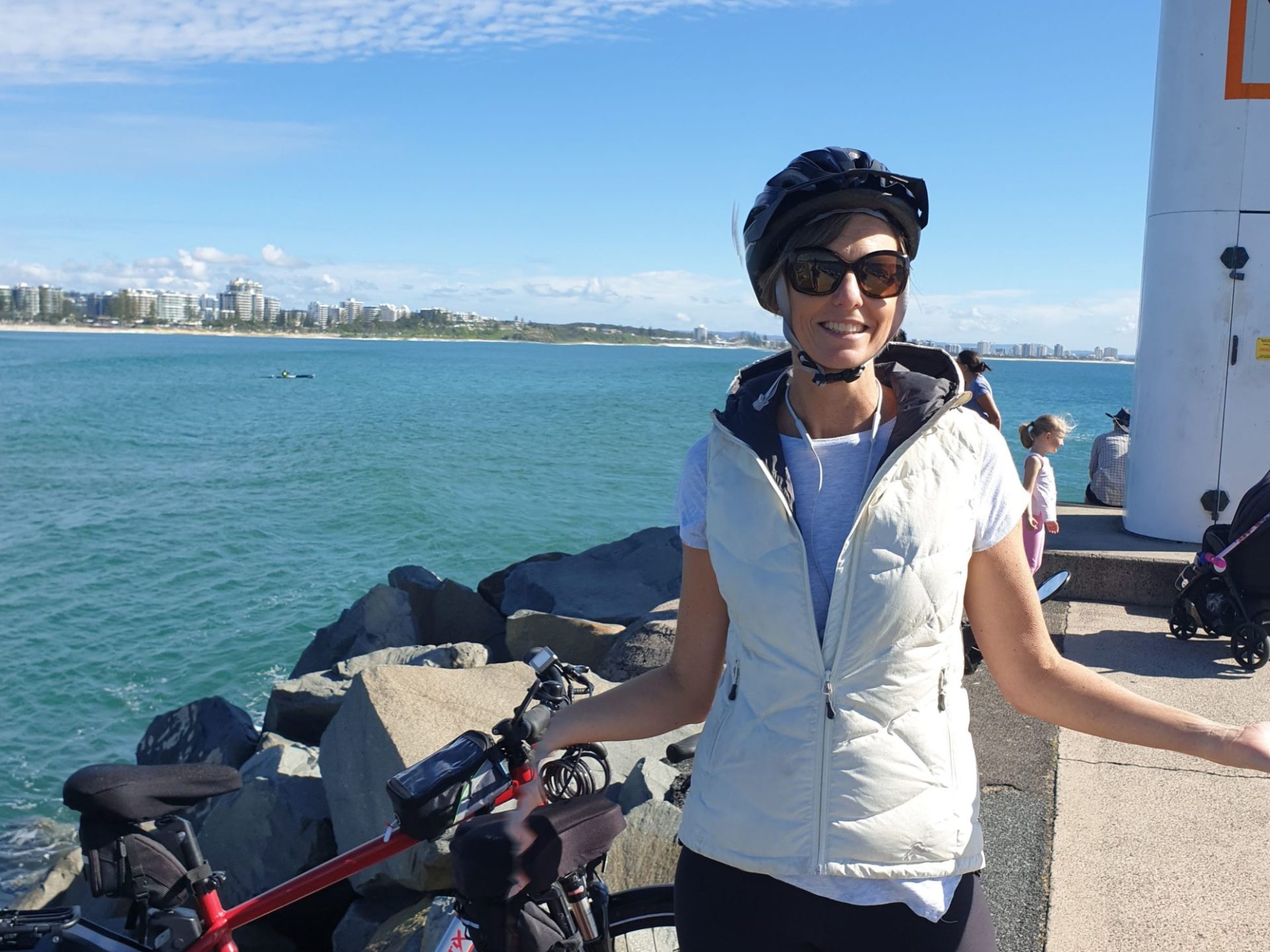 An e-bike rider beams with joy on the River to River Tour at the Mooloolaba Spit Rock Wall, overlooking the turquoise blue waters of Mooloolaba Bay and the Alex Heads skyline in the distance.