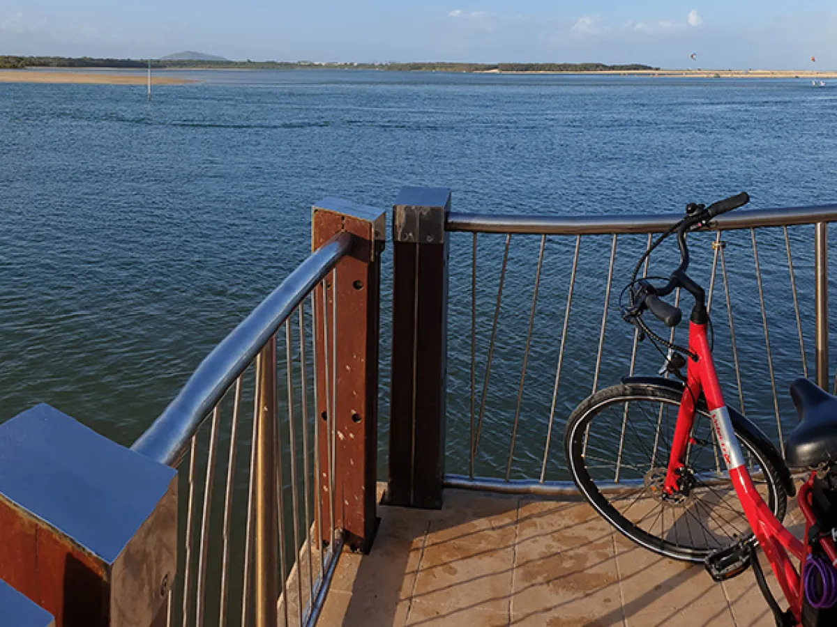 Two EcoTekkSC e-bikes parked on the Cotton Tree outlet pier with the mouth of the Maroochy River in the background, bathed in afternoon sunlight.