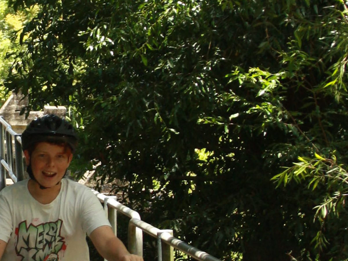 A family rides EcoTekkSC-hired e-bikes with big smiles while crossing the old Cobb and Co Lane footbridge over the South Maroochy River at Crows Park, Yandina, QLD. Dad tows a child trailer with his granddaughter, returning from the Yandina Ginger Factory.