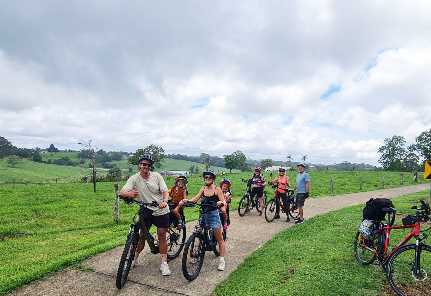 Family on e-MTBs with two girls in child seats and cyclists enjoying views of rolling pastures after a hill climb on the Maleny Magic Tour