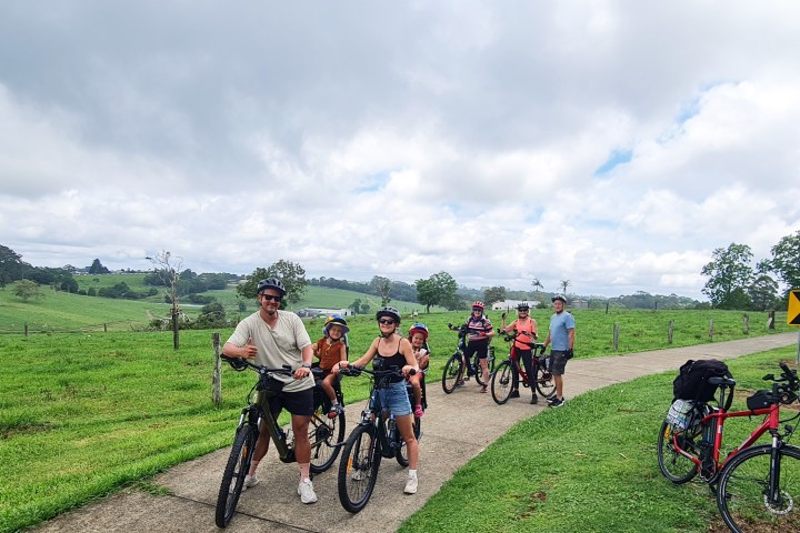 Family on e-MTBs with two girls in child seats and cyclists enjoying views of rolling pastures after a hill climb on the Maleny Magic Tour