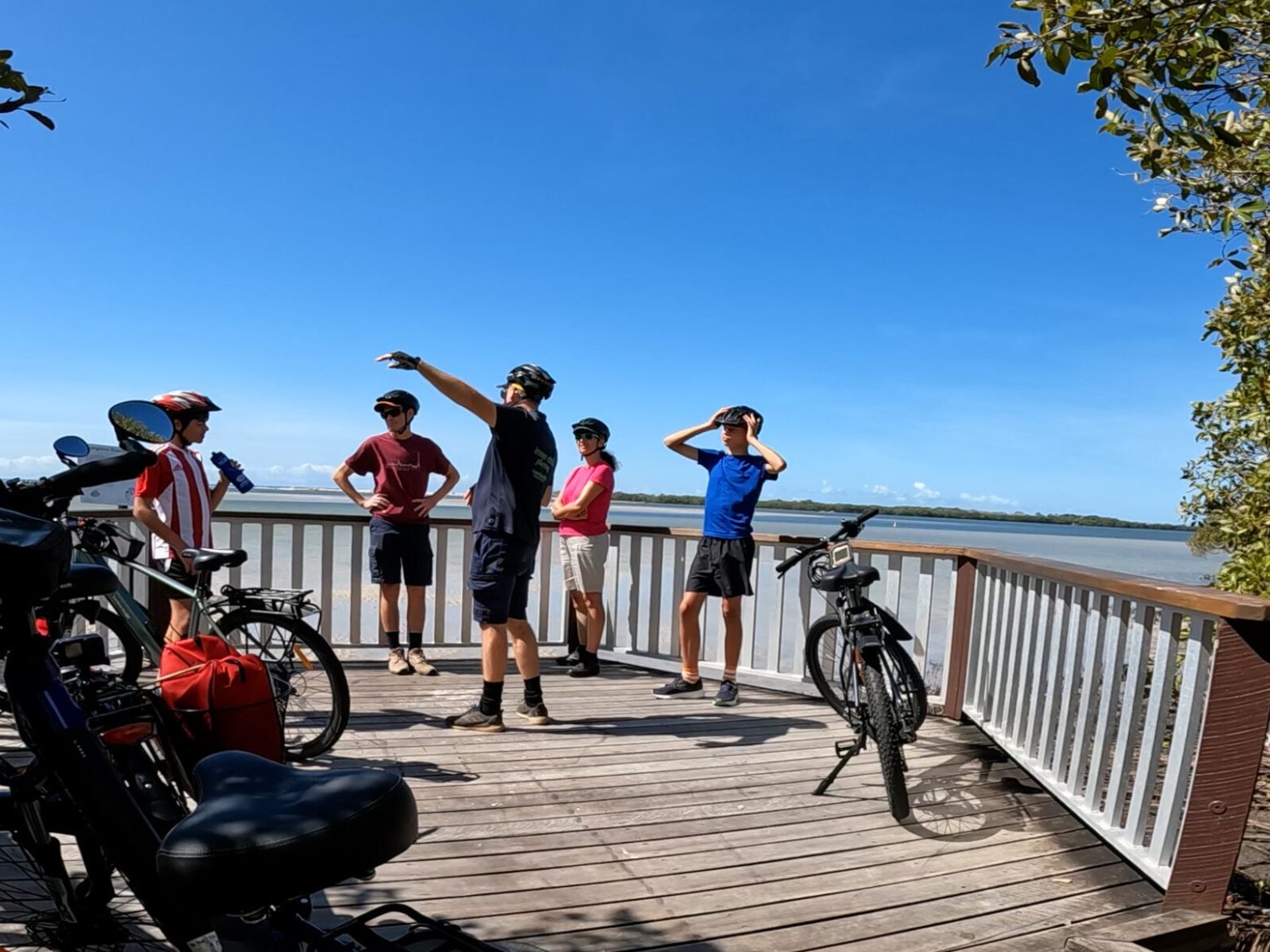 Family of four with EcoTekk Sunshine Coast guide on the Golden Beach e-bike tour, standing on Murray's Beach Mangrove Boardwalk, learning about the environmental significance of Pumicestone Passage.