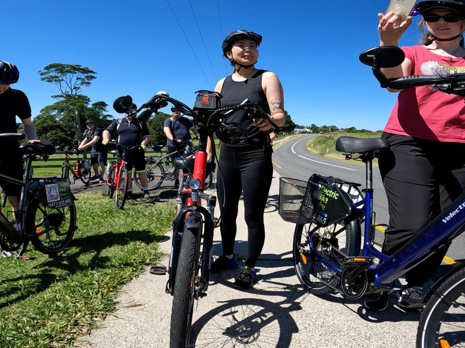 Group of friends and family on e-bikes smiling while overlooking the Glasshouse Mountains at One Tree Hill on the Maleny Magic e-Bike Tour.