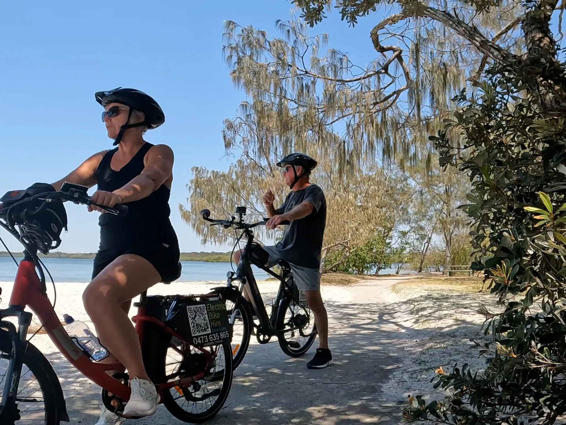 A couple on an ecoTekkSC e-bike tour, admiring the stunning views across Pumicestone Passage at Golden Beach, Caloundra, towards Bribie Island National Park.