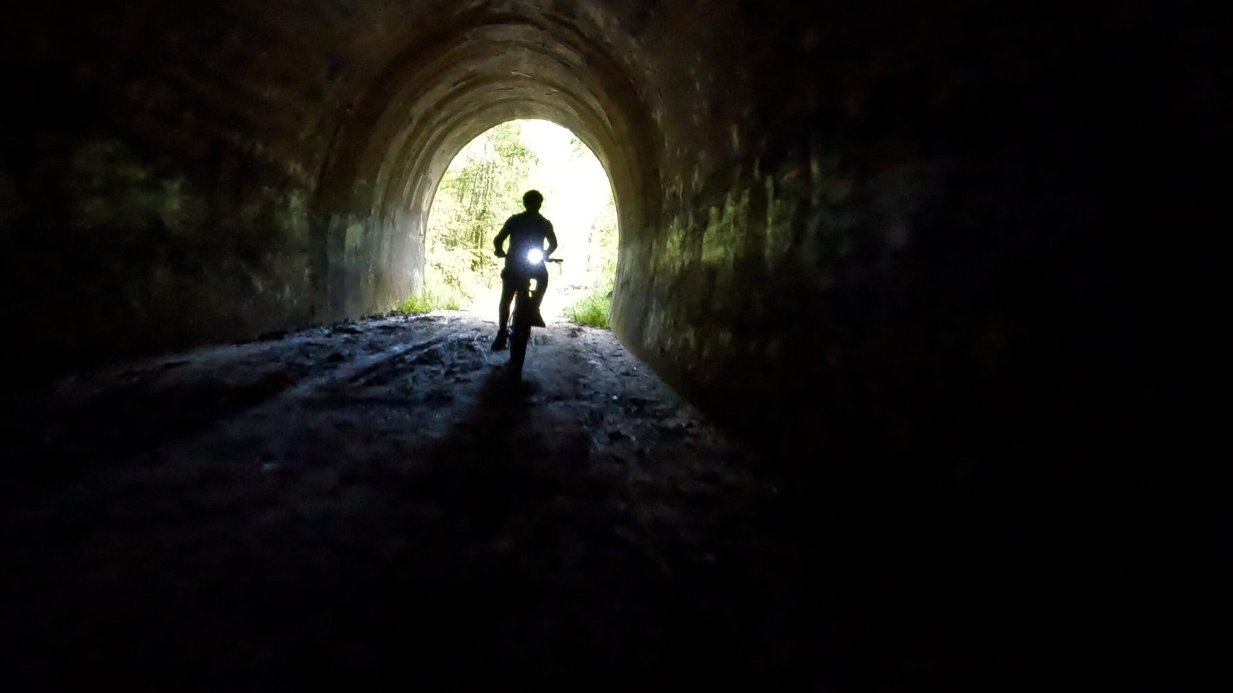 Silhouetted e-MTB rider entering the Dularcha Railway Tunnel, with the northern arch entrance illuminated by background light.