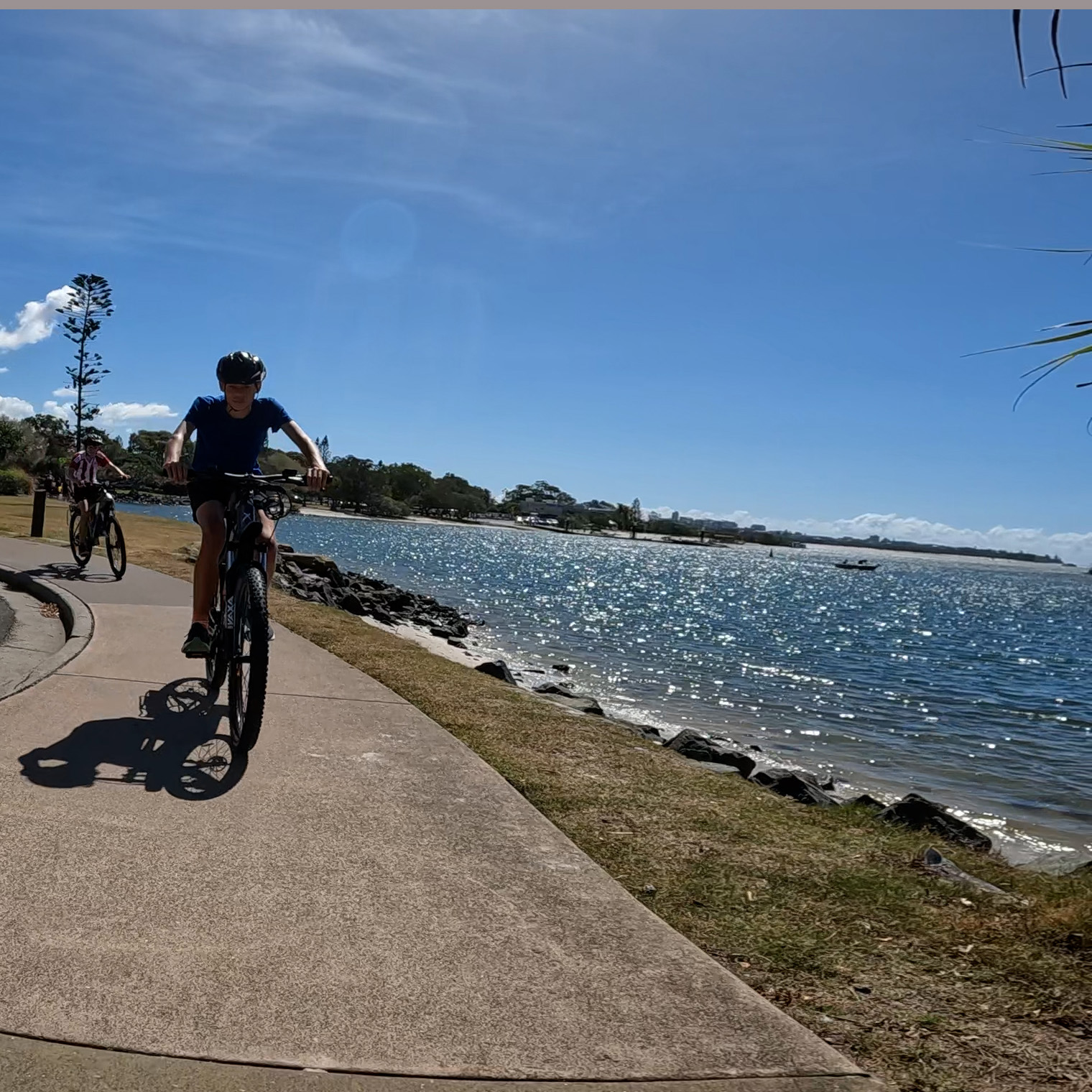 Teenagers Enjoying Golden Beach e-bike Tour – Pumicestone Passage Views Two teenage boys riding e-MTBs on the ecoTekk Sunshine Coast Golden Beach tour, approaching Military Jetty with views of Caloundra across the turquoise waters of Pumicestone Passage.