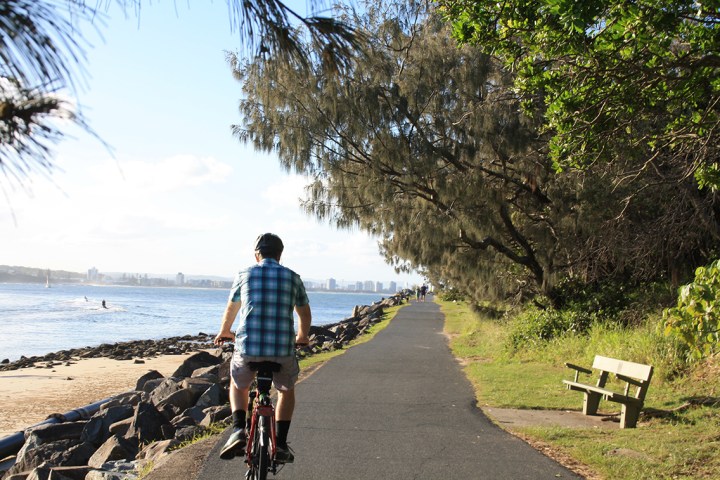 e-Bike rider enjoys sunset ride along Pt Cartwright rock wall with Maroochydore skyline backdrop