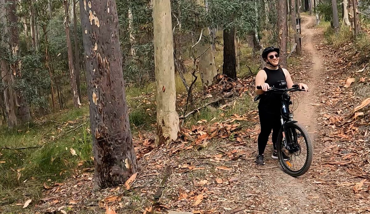 Smiling woman riding an e-MTB mid-trail on Cooroora Trail during her first mountain biking adventure.