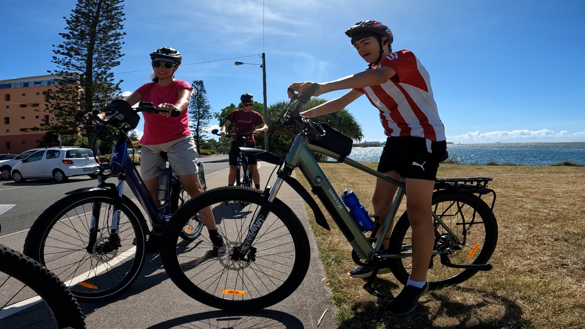 Family with teenage boys riding e-bikes beside the glittering waters of Pumicestone Passage on ecoTekk’s Golden Beach Tour