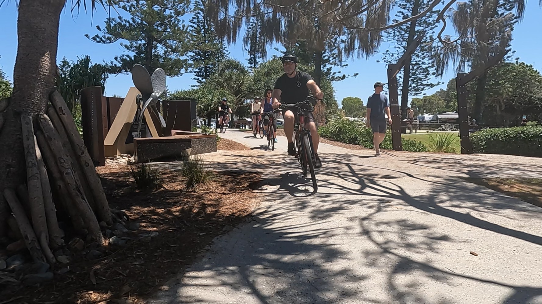 Four ecoTekkSC e-bike riders passing Dicky Beach Skate Park and the S.S. Dicky propeller