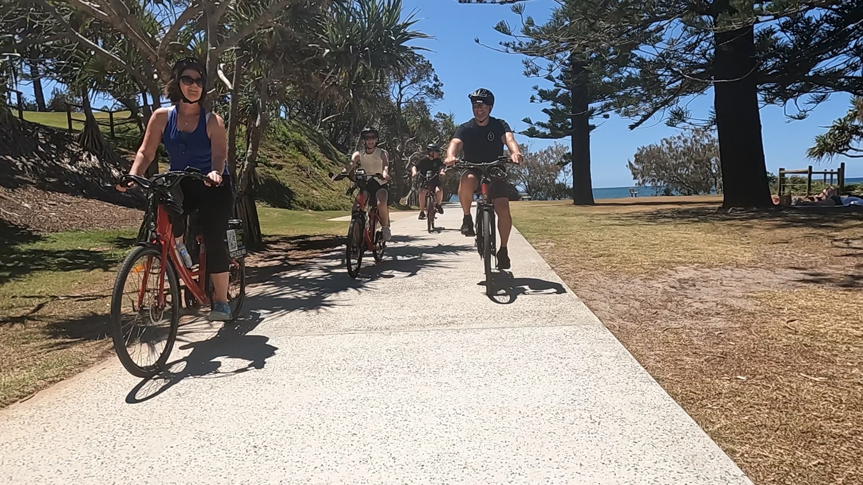 Four ecoTekkSC e-bike riders abreast at Sir Leslie Wilson Park, Dicky Beach with ocean views